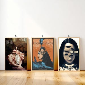 May include: Three framed movie posters with the title "Poor Things". The posters feature different artistic designs, including a woman in a pink dress, a woman with blue and orange tones, and a woman with multiple eyes. The posters are in wooden frames.