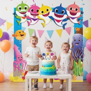 Op de afbeelding: Een verjaardagssc&egrave;ne met drie kinderen, een taart en haai-thema decoraties. De taart is blauw en groen met haai-toppers. Kleurrijke ballonnen en zeedier-uitsparingen maken de feestelijke setting compleet.