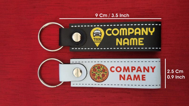 K&ouml;nnte beinhalten: Zwei Schl&uuml;sselanh&auml;nger, einer schwarz und einer wei&szlig;, mit silbernen Ringen. Der schwarze Schl&uuml;sselanh&auml;nger hat eine Taxi-Grafik und die Worte "COMPANY NAME". Der wei&szlig;e Schl&uuml;sselanh&auml;nger zeigt eine Pizza-Grafik und die Worte "COMPANY NAME". Die Schl&uuml;sselanh&auml;nger sind 9 cm lang und 2,5 cm breit.