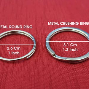 K&ouml;nnte beinhalten: Zwei silberne Metallringe auf rotem Hintergrund. Der kleinere Ring, beschriftet mit "METAL ROUND RING", misst 2,6 cm (1 Zoll) im Durchmesser. Der gr&ouml;&szlig;ere Ring, "METAL CRUSHING RING", hat einen Durchmesser von 3,1 cm (1,2 Zoll).