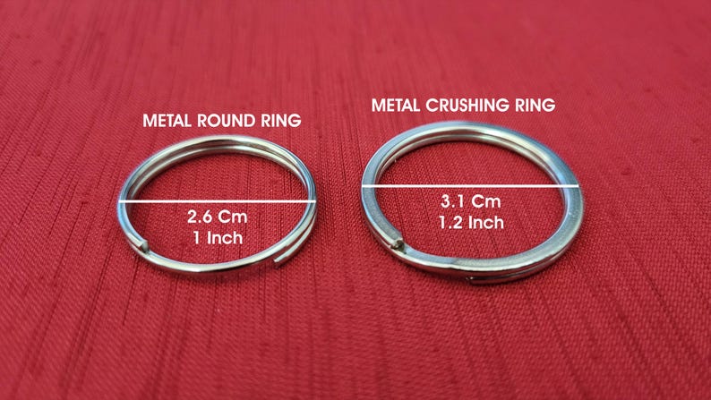 K&ouml;nnte beinhalten: Zwei silberne Metallringe auf rotem Hintergrund. Der kleinere Ring, beschriftet mit "METAL ROUND RING", misst 2,6 cm (1 Zoll) im Durchmesser. Der gr&ouml;&szlig;ere Ring, "METAL CRUSHING RING", hat einen Durchmesser von 3,1 cm (1,2 Zoll).