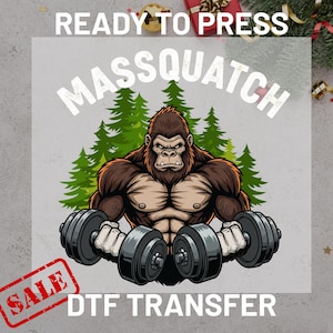 May include: A DTF transfer featuring a cartoon gorilla lifting dumbbells, with the text "MASSQUATCH" above and "DTF TRANSFER" below. The image includes green pine trees and a "SALE" stamp.