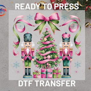 May include: A DTF transfer design featuring a Christmas theme. The design includes two nutcracker figures, a decorated Christmas tree, wrapped gifts, and a large pink bow. The words "READY TO PRESS" and "DTF TRANSFER" are displayed.
