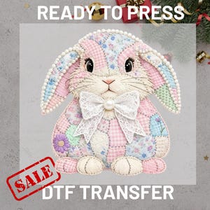 May include: A patchwork bunny DTF transfer with a white lace bow and pearl accent. The bunny is in shades of pink, blue, and green, with the words "READY TO PRESS" and "SALE" visible.