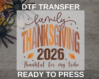 May include: A DTF transfer sheet featuring the text DTF TRANSFER, READY TO PRESS, and a graphic design with the words family THANKSGIVING 2026 Thankful for my tribe in brown, orange, and tan colors, accented with small stars and two orange leaves.