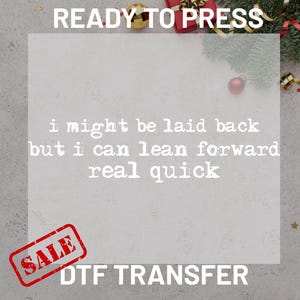 May include: A DTF transfer with the text "READY TO PRESS" at the top. The text "i might be laid back but i can lean forward real quick" is in the center. A red "SALE" stamp is in the lower left.