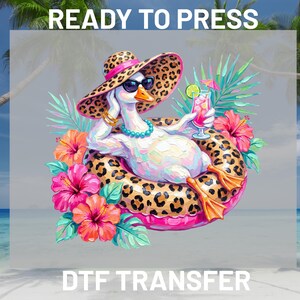 May include: A Ready to Press DTF transfer featuring a white goose wearing a leopard print sun hat, sunglasses, and a turquoise necklace. The goose floats in a leopard print inner tube, holding a pink cocktail with a lime slice and umbrella.