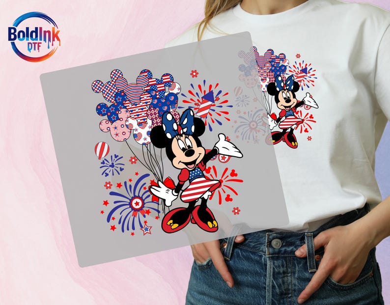 K&ouml;nnte beinhalten: Ein wei&szlig;es T-Shirt mit einem Grafikdruck von Minnie Maus in einem patriotischen rot-wei&szlig;-blauen Outfit. Das Design zeigt Mickey-f&ouml;rmige Luftballons mit Sternen- und Streifenmustern, rote und blaue Feuerwerke sowie das BoldInk DTF-Logo.
