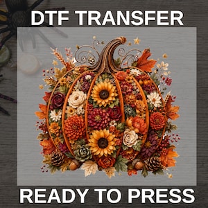 May include: A DTF TRANSFER READY TO PRESS graphic featuring a central pumpkin filled with autumn-colored flowers, including yellow sunflowers, orange dahlias, and red roses, accented with brown pinecones, acorns, and maple leaves on a dark background.