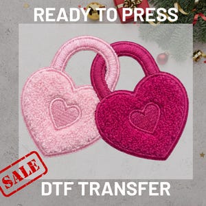 May include: Two heart-shaped DTF transfers, one light pink and one magenta, interlocked. Each has a smaller heart in the center and a handle. The words "READY TO PRESS" and "DTF TRANSFER" are displayed. A "SALE" stamp is in the corner.