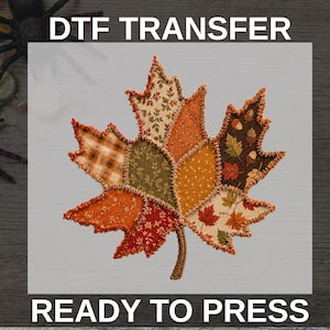 May include: A DTF TRANSFER READY TO PRESS graphic featuring a large maple leaf composed of various fabric-like patches in autumn colours including orange, brown, green, and cream with plaid, floral, and acorn patterns and a decorative stitched edge.