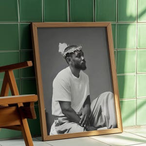 May include: A framed black and white portrait of a person wearing a crown of thorns, seated and looking to the side. The portrait is in a wooden frame, leaning against a green tiled wall. A wooden chair is in the foreground.