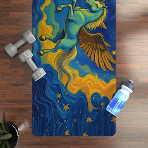 May include: A rectangular yoga mat featuring a blue and yellow unicorn design. The artwork depicts a winged unicorn in a starry sky. A pair of gray dumbbells and a water bottle are visible on the wooden floor.