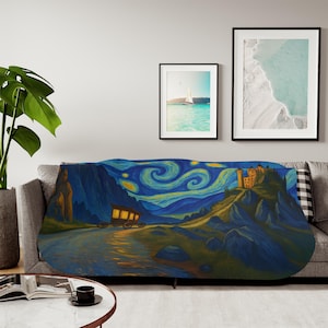 Può includere: Una coperta decorativa su un divano grigio, con una rappresentazione artistica di un paesaggio notturno con cieli blu e gialli vorticosi, una strada e una carrozza. L'opera d'arte ricorda un famoso dipinto.