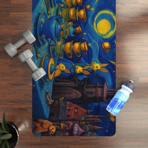 May include: A yoga mat with a whimsical design depicting teacups, rabbits, and a starry night sky in blue, yellow, and gold. Two grey dumbbells and a water bottle are also visible.
