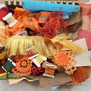 May include: A box filled with craft materials, featuring fabric remnants in orange, red, and brown, plus spools of thread and lace. A blue tulle fabric is visible at the top. Suitable for sewing and crafting projects.