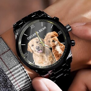 May include: A black wristwatch with a metal link band featuring a custom dial with the text OSCAR & BEAR and a photographic print of a golden retriever and a small brown dog. The watch has gold-tone hands and Roman numeral hour markers.