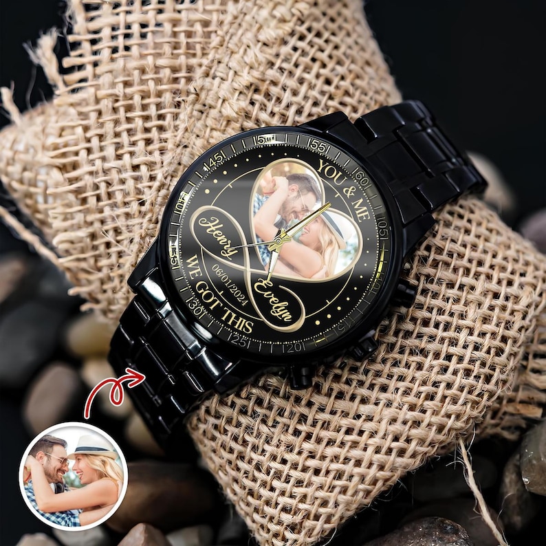 May include: A black metal wristwatch with a custom dial featuring a heart-shaped photo of a couple, the names Henry and Evelyn, the date 06/01/2024, and the text YOU & ME and WE GOT THIS. The watch has a black link band and gold-tone hands.