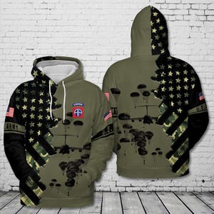 May include: Olive green hoodie with a design featuring a U.S. flag, stars, and camouflage. The hoodie has a front pocket, a hood, and the word "ARMY" on the sleeve. The design includes parachutes and the Airborne insignia.