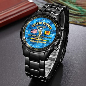 May include: Black wristwatch with a blue face featuring the text "Vietnam Veteran 1965-1966". The watch face includes the American and South Vietnamese flags. The watch band and case are black.