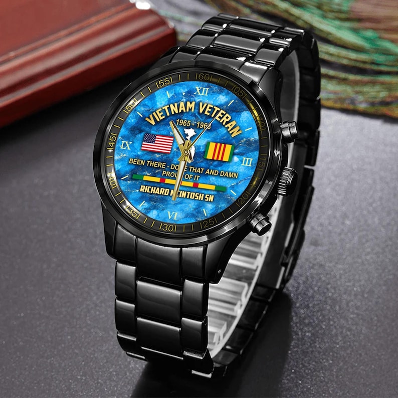 May include: Black wristwatch with a blue face featuring the text "Vietnam Veteran 1965-1966". The watch face includes the American and South Vietnamese flags. The watch band and case are black.