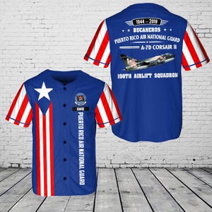 May include: A blue baseball jersey with red and white striped sleeves. The front features a white star and the Puerto Rican flag design. The back displays text: "1944-2019 BUCANEROS PUERTO RICO AIR NATIONAL GUARD A-7D CORSAIR II 198TH AIRLIFT SQUADRON."