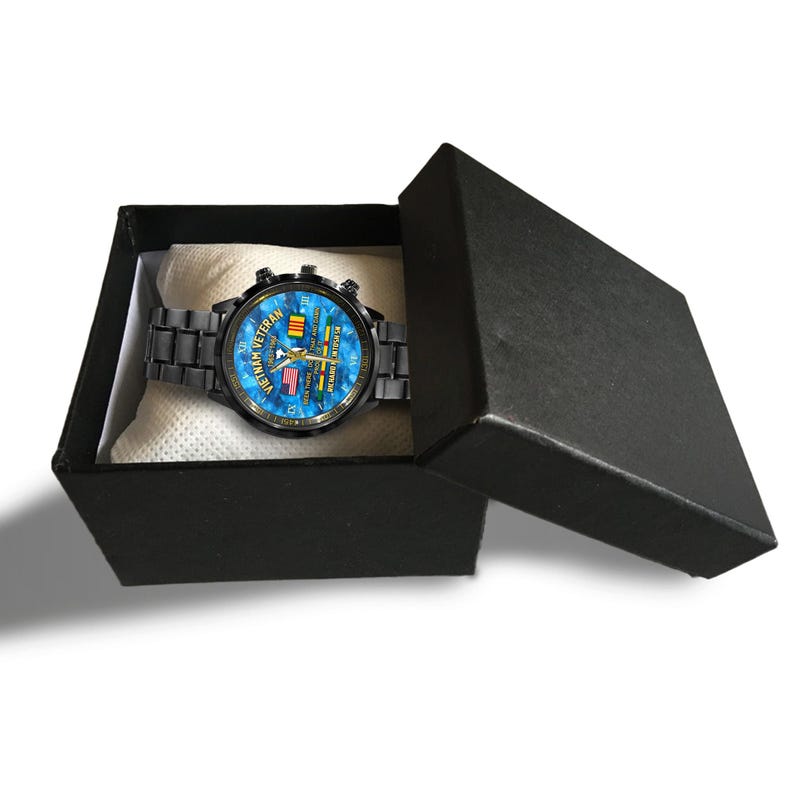 May include: A black wristwatch with a blue face featuring the text "Vietnam Veteran" and flags. The watch is in a black box with a white interior. The watch band is black.