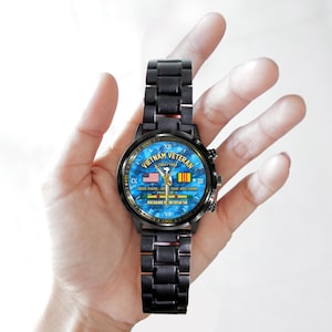 May include: Black wristwatch with a blue face featuring the text "Vietnam Veteran 1965-1968". The watch face includes the American and Vietnamese flags. The watch band is black.