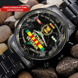 May include: Black wristwatch with a marble-effect face, featuring the words "Vietnam Veteran" and the years "1960-1975." The watch face includes military emblems and the text "All Gave Some, 58479 Gave All." The watch has a black metal band.