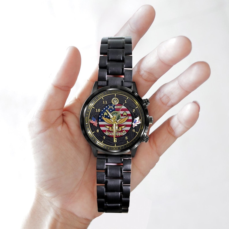 May include: A black metal wristwatch with a round face featuring a U.S. Army emblem, an American flag background, and the word VETERAN printed in gold. The watch has gold-coloured hands, numerical hour markers, and a black link bracelet strap.