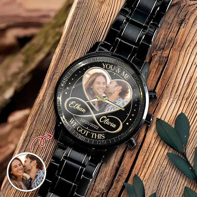 May include: A black metal wristwatch with a circular face featuring a heart-shaped photo of a couple, the names Ethan and Olivia, an infinity symbol, the date 10/25/2022, and the text YOU & ME and WE GOT THIS printed on the black dial.