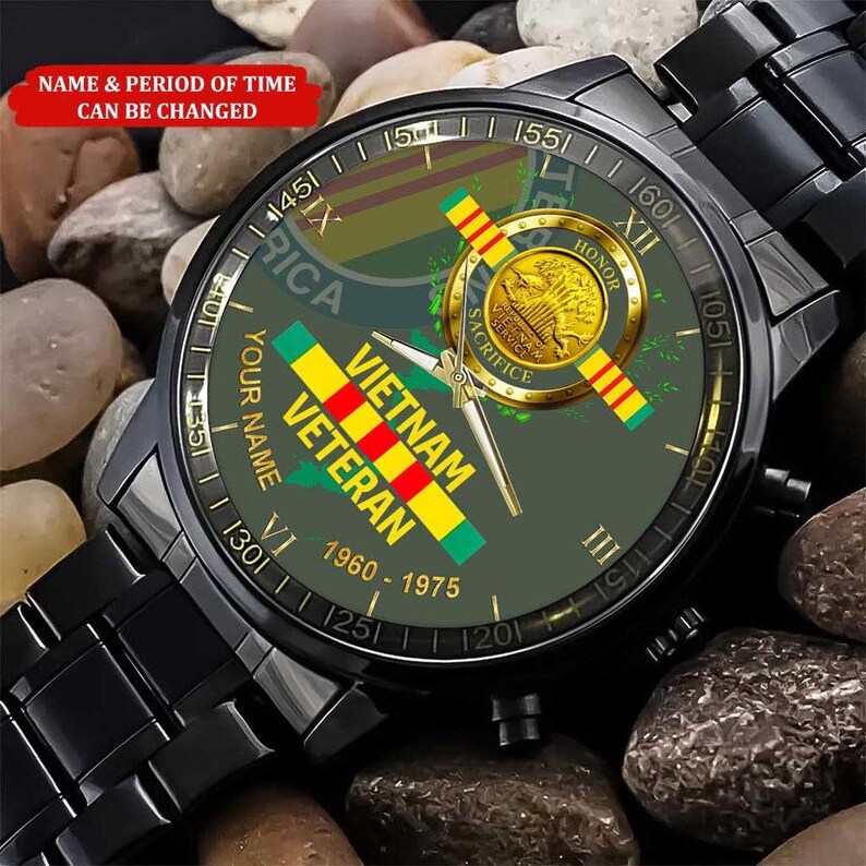 Puede incluir: Reloj de pulsera negro con esfera verde con un dise&ntilde;o de Veterano de Vietnam. La esfera incluye el texto "Vietnam Veteran" y "1960-1975", junto con un emblema dorado y una correa negra. El reloj se muestra sobre un lecho de peque&ntilde;as piedras.