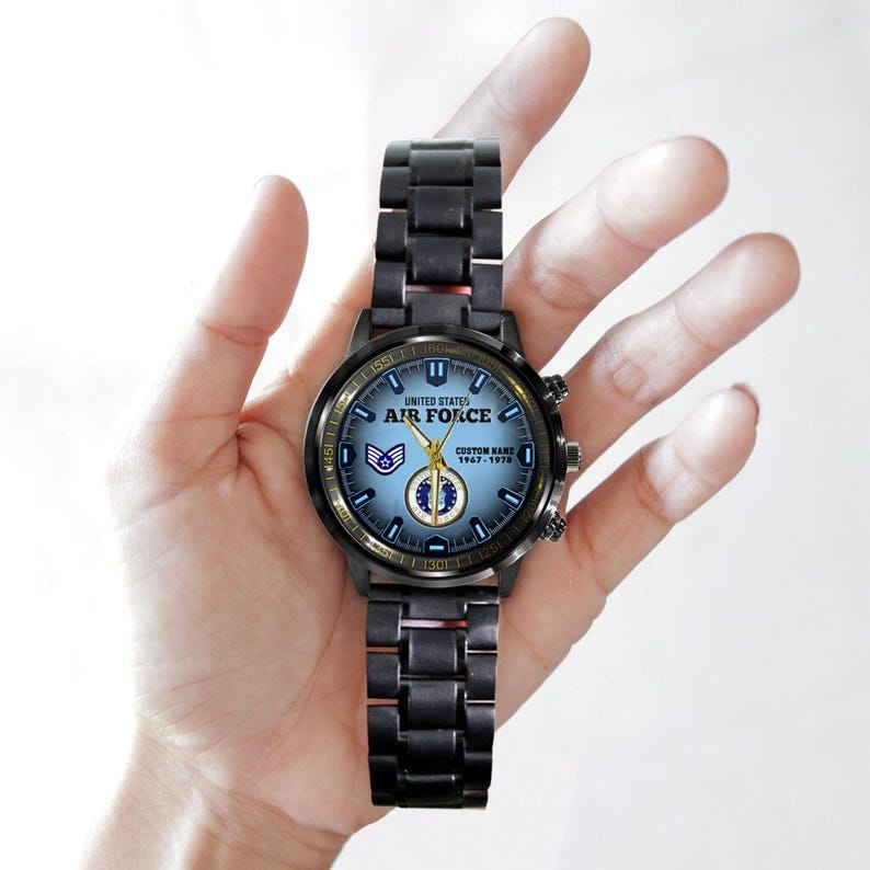 May include: A black metal wristwatch with a light blue dial featuring the text United States Air Force, a military emblem, and the custom text Custom Name 1967-1978. The watch has a link bracelet, gold-coloured hands, and a circular case.