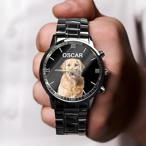 May include: A black metal wristwatch with a link band and a round face. The watch dial features a golden retriever dog portrait in the center, the name OSCAR printed in white above the dog, and Roman numerals for the hour markers on the edge.