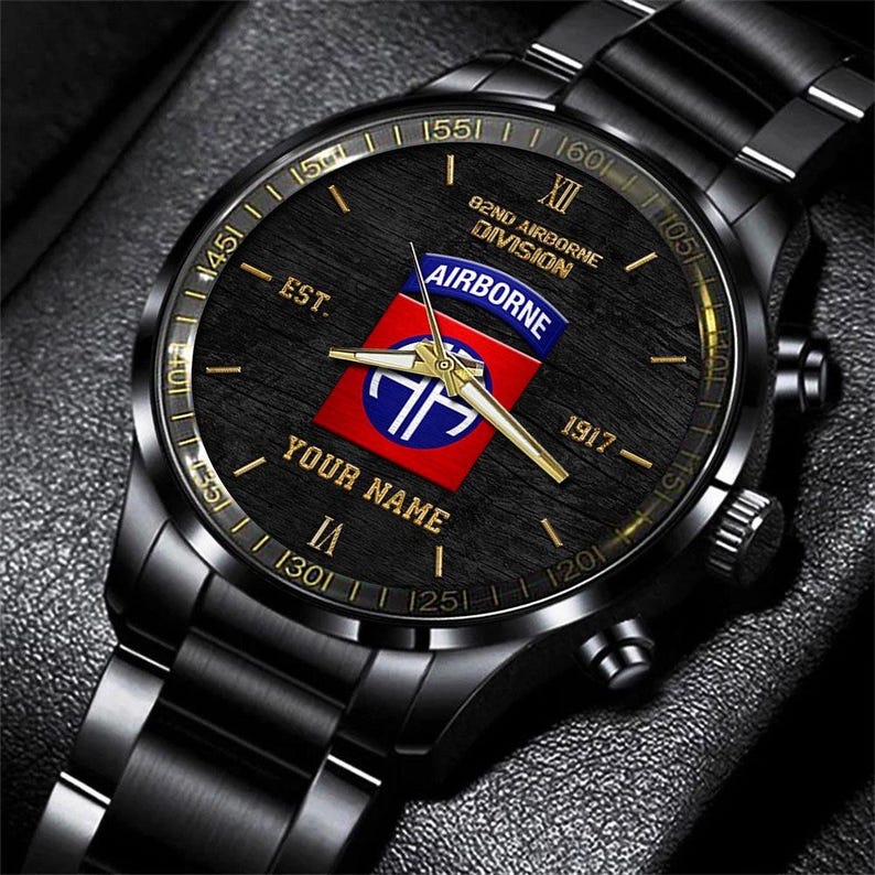 May include: Black wristwatch with a black face and band. The watch face features gold numerals and hands, with the text "YOUR NAME" and a red, white, and blue emblem that reads "AIRBORNE". The watch also has the text "82ND AIRBORNE DIVISION" and "EST. 1917".
