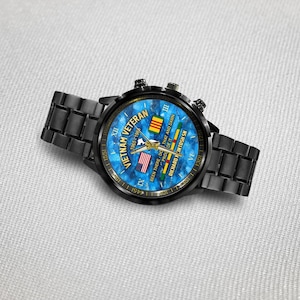 May include: Black wristwatch with a blue face featuring the text "Vietnam Veteran 1965-196" and the American and Vietnamese flags. The watch has a black metal band and a black bezel. The watch also has the text "Been there, done that and damn proud of it."