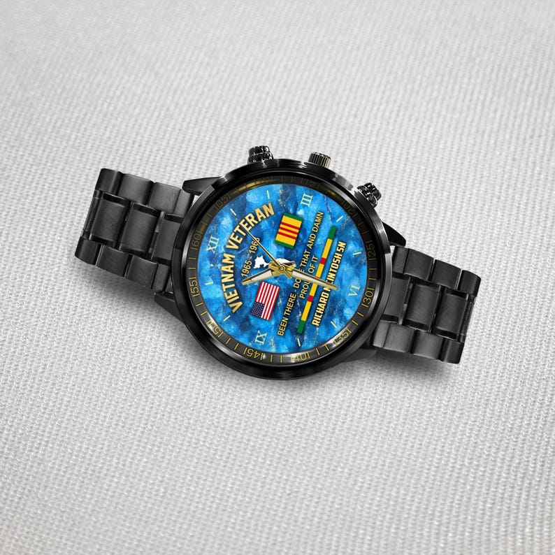 May include: Black wristwatch with a blue face featuring the text "Vietnam Veteran 1965-196" and the American and Vietnamese flags. The watch has a black metal band and a black bezel. The watch also has the text "Been there, done that and damn proud of it."