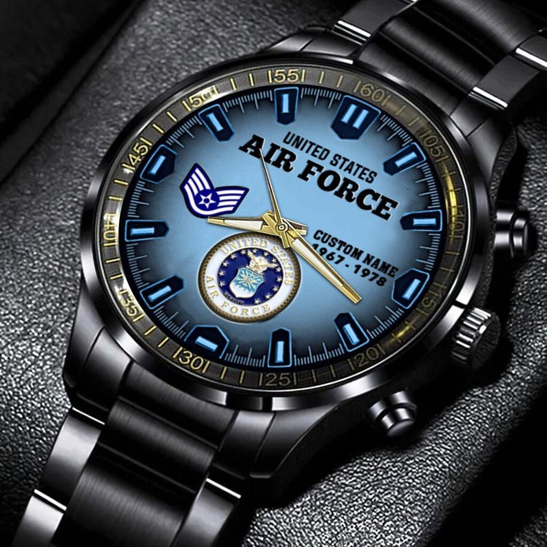 May include: A black stainless steel wristwatch with a light blue dial featuring the United States Air Force emblem, the text UNITED STATES AIR FORCE, CUSTOM NAME, and 1967-1978. The watch has gold-toned hands and a black metal link bracelet.