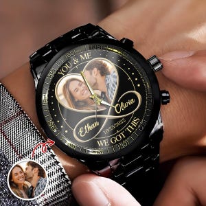 May include: A black wristwatch with a custom photo dial featuring a couple inside a gold heart and infinity symbol. The watch face displays the text YOU & ME, Olivia, Ethan, 10/25/2022, and WE GOT THIS in gold lettering with gold hands.