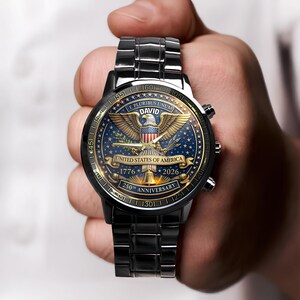 May include: A black wristwatch with a detailed face featuring a golden eagle, the text "E PLURIBUS UNUM", and "UNITED STATES OF AMERICA". The watch commemorates the 250th anniversary, with dates 1776 and 2026. The watch band is also black.