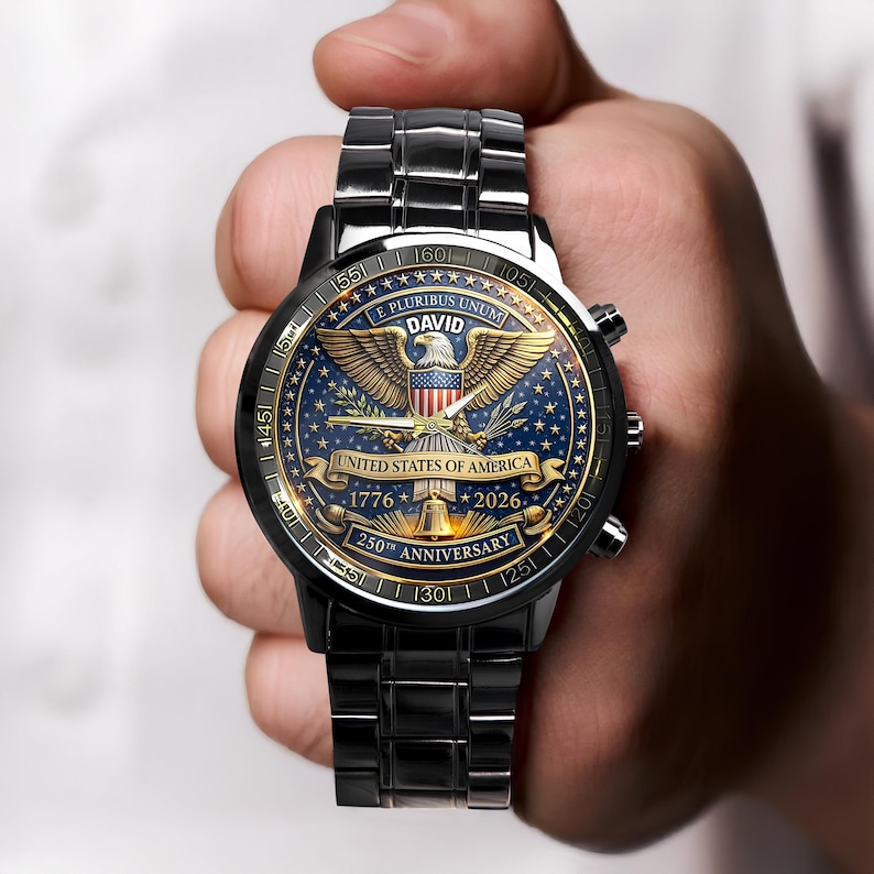 May include: A black wristwatch with a detailed face featuring a golden eagle, the text "E PLURIBUS UNUM", and "UNITED STATES OF AMERICA". The watch commemorates the 250th anniversary, with dates 1776 and 2026. The watch band is also black.