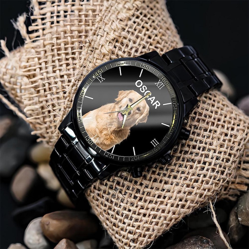 May include: A black metal wristwatch with a black dial featuring a golden retriever portrait and the name OSCAR printed in white. The watch has a black link band, gold-toned hour, minute, and second hands, and Roman numeral hour markers.