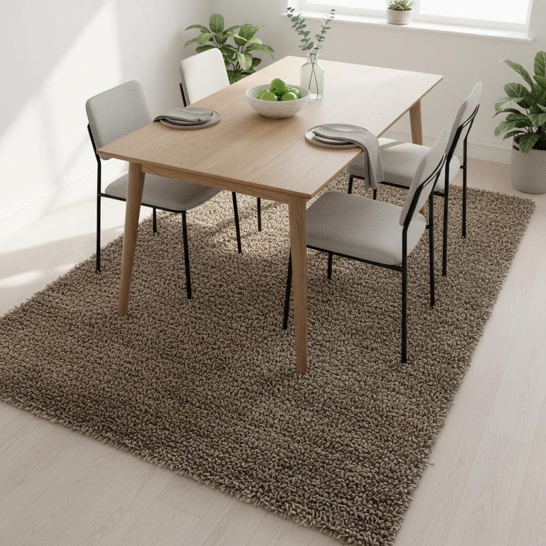 May include: A dining room set with a light wood table and four gray chairs with black legs. The table is set with plates, napkins, and a bowl of green apples. A shaggy brown rug covers the floor.