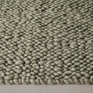 Puede incluir: Primer plano de una alfombra texturizada verde salvia. La superficie de la alfombra está densamente cubierta de bucles redondeados y elevados, creando un efecto táctil y tridimensional. El color es un verde apagado y terroso, adecuado para varios estilos de interior.