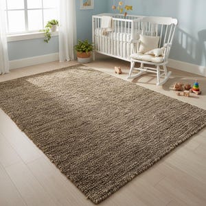 May include: A large, rectangular, neutral-toned rug with a textured surface. The rug is placed on a light-colored wooden floor in a nursery setting, with a white crib, rocking chair, and toys visible in the background.