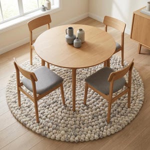 Puede incluir: Una mesa de comedor de madera clara con cuatro sillas a juego, cada una con asiento gris. La mesa est&aacute; sobre una alfombra redonda y texturizada en tonos blancos y grises. Jarrones decorativos sobre la mesa.
