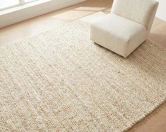 Peut inclure: Un grand tapis rectangulaire tissé blanc cassé avec une surface texturée. Une petite chaise rembourrée de couleur crème est posée sur le tapis. Le tapis est posé sur un parquet clair près d'une fenêtre.