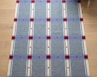 May include: A rectangular area rug featuring a grid pattern of light blue and slate blue squares. The design includes vertical and horizontal white stripes intersecting at small, solid red squares, with tiny red dots centered in each blue square.