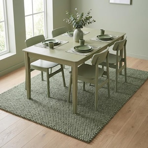 May include: A sage green dining room set featuring a rectangular table, four chairs, and a textured rug. The table is set with plates, cups, and placemats. A vase of greenery sits in the center. The rug is approximately 152 cm by 228 cm.