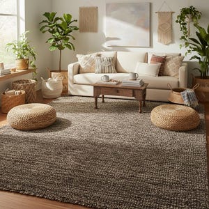 May include: A living room scene featuring a neutral-toned sofa with decorative pillows, a wooden coffee table, and a large, textured area rug. Woven baskets and potted plants add natural elements. Two round woven ottomans sit on the rug, enhancing the cozy atmosphere.